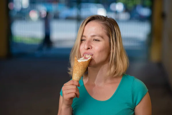 Ritratto di una ragazza carina in un vestito verde è camminare fuori e mangiare dessert. Bella bionda che si gode un cono con gelato in una bella giornata estiva. La vita è un piacere — Foto Stock