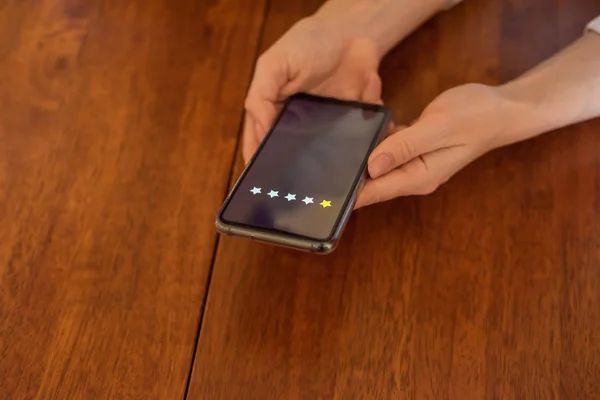 Mujer votar en un teléfono inteligente mientras está sentado en la mesa. Las manos sosteniendo el teléfono y organizar la calificación, Una estrella. Experiencia. Primer plano del teléfono — Foto de Stock