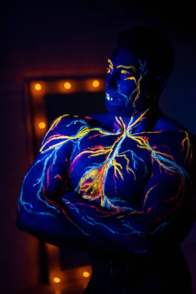 Padrões UV arte corporal do sistema circulatório no corpo de um homem. No tronco de um atleta muscular, veias e artérias são desenhadas com corantes fluorescentes. Fisiculturista em pé junto ao espelho com lâmpadas . — Fotografia de Stock