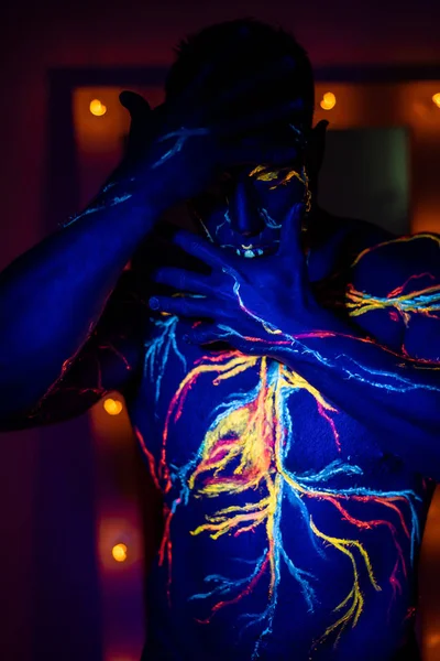 Modelli UV body art del sistema circolatorio sul corpo di un uomo. Sul busto di un atleta muscolare, vene e arterie sono disegnate con coloranti fluorescenti. Bodybuilder in piedi accanto allo specchio con lampade . — Foto Stock