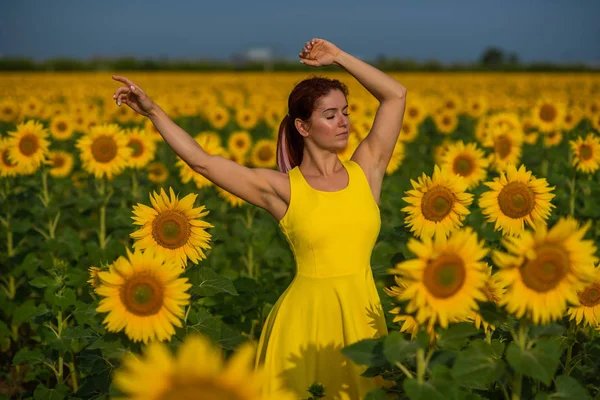 Eine rothaarige Frau in einem gelben Kleid steht auf einem Sonnenblumenfeld. schöne Mädchen im Rock Sonne genießt einen wolkenlosen Tag auf dem Land. rosa Haarsträhnen. — Stockfoto