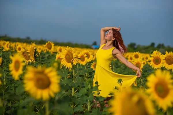 Eine rothaarige Frau in einem gelben Kleid steht auf einem Sonnenblumenfeld. schöne Mädchen im Rock Sonne genießt einen wolkenlosen Tag auf dem Land. rosa Haarsträhnen. — Stockfoto