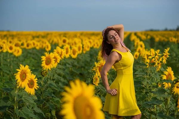 一个穿着黄色衣服的红头发的女人站在向日葵的田野里。穿着裙子的漂亮女孩在乡下享受无云的一天。头发的粉红色锁. — 图库照片