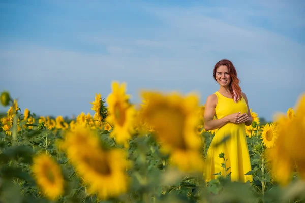 Eine rothaarige Frau in einem gelben Kleid steht auf einem Sonnenblumenfeld. schöne Mädchen im Rock Sonne genießt einen wolkenlosen Tag auf dem Land. rosa Haarsträhnen. — Stockfoto