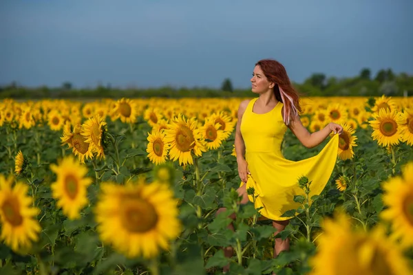 Eine rothaarige Frau in einem gelben Kleid steht auf einem Sonnenblumenfeld. schöne Mädchen im Rock Sonne genießt einen wolkenlosen Tag auf dem Land. rosa Haarsträhnen. — Stockfoto