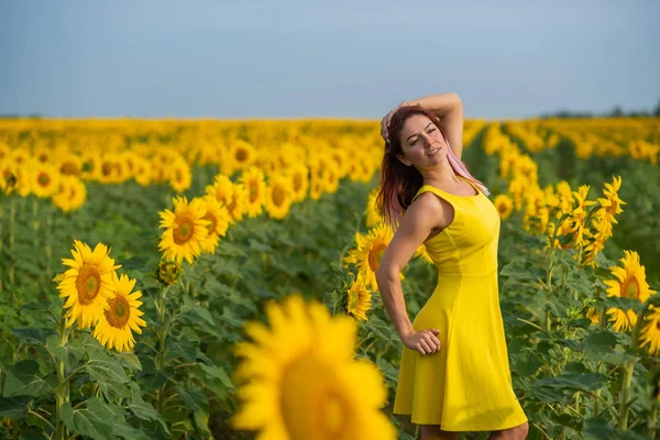 Eine rothaarige Frau in einem gelben Kleid steht auf einem Sonnenblumenfeld. schöne Mädchen im Rock Sonne genießt einen wolkenlosen Tag auf dem Land. rosa Haarsträhnen. — Stockfoto
