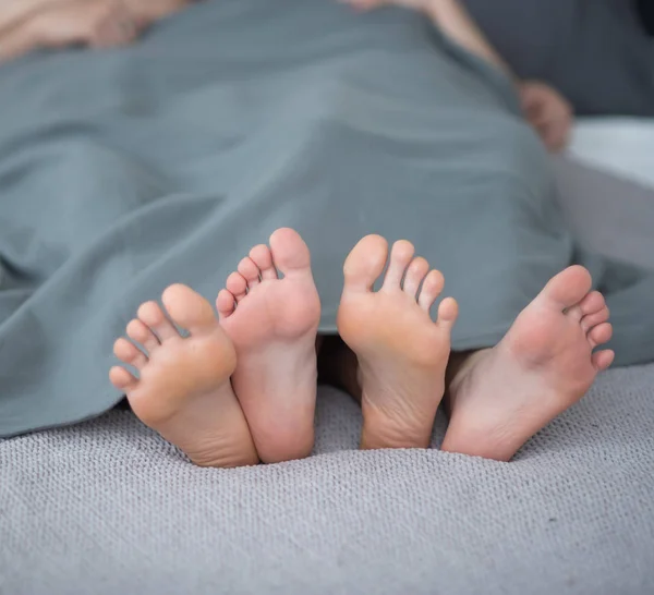 Gros plan des jambes masculines et féminines. Le couple aimant se couche et s'embrasse sur le lit sous une couverture grise. Salle lumineuse . — Photo
