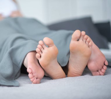 Erkek ve dişi bacakların yakın çekim. Sevgi dolu çift yalan ve gri bir battaniye altında yatakta kucaklar. Işık odası.