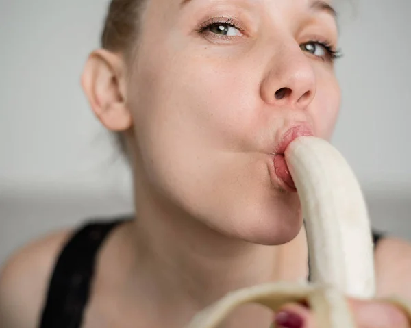 Primo piano del viso, labbra, lingua di una giovane ragazza europea che lecca una grande banana gialla e dolce . — Foto Stock