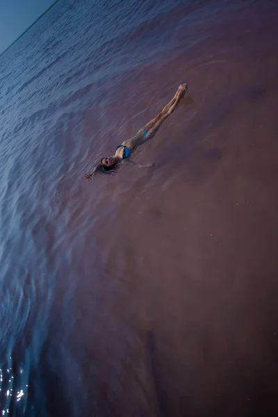 Une femme en bikini bleu nage sur le dos dans un lac salé. Miracle de la nature lac rose. Dépôt et extraction de sel. Eau dense poussant à la surface. Procédures thérapeutiques dans l'eau minérale . — Photo