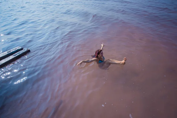 Une femme nage sur le dos dans un lac salé et rit. Miracle de la nature lac rose. Dépôt et extraction de sel. Eau dense poussant à la surface. Procédures thérapeutiques dans l'eau minérale — Photo