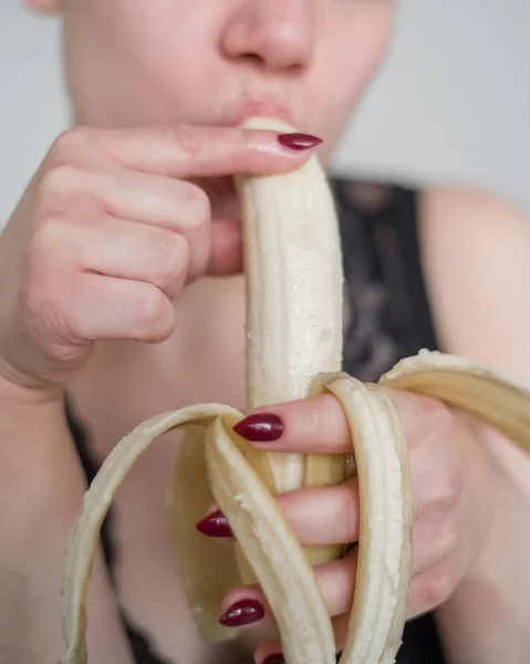 Närbild av ansiktet, läppar, tungan av en ung, europeisk flicka slickar en stor gul, Söt banan. — Stockfoto