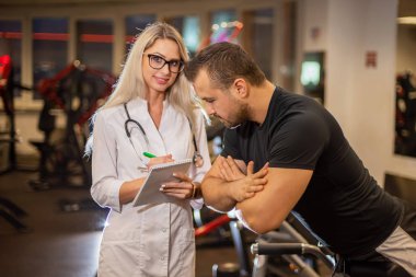 Tıbbi muayene. Doktor stres testi sırasında nabzı ölçer. Kadın bir doktor koşu bandında erkek atletlerin kalp atışlarını ölçer..