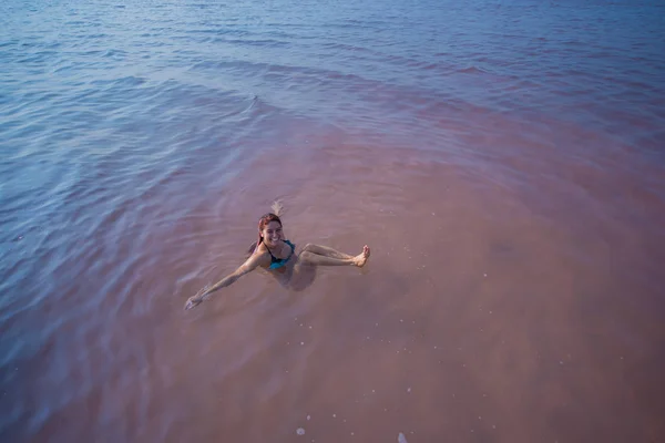 Une femme nage sur le dos dans un lac salé et rit. Miracle de la nature lac rose. Dépôt et extraction de sel. Eau dense poussant à la surface. Procédures thérapeutiques dans l'eau minérale — Photo