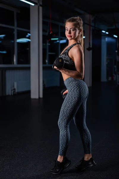 Vacker muskulös ung kvinna gör övningar med hantlar i gymmet. Flickan arbetar ut musklerna i armarna med en hantel. Kvinnlig Bodybuilder tåg biceps och triceps — Stockfoto