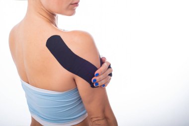 Beyaz arka planda Kineziotape bandı olan bir bayan omuz. Eklemlerde ve bağlarda spor sakatlıkları için alternatif tıp. Omzunda siyah bir bantla genç bir sporcu..