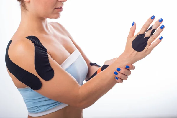 Female shoulder with kineziotape on a white background. Alternative medicine for sports injuries of joints and ligaments. Sportswoman with a black medical record on a sore shoulder and middle finger.