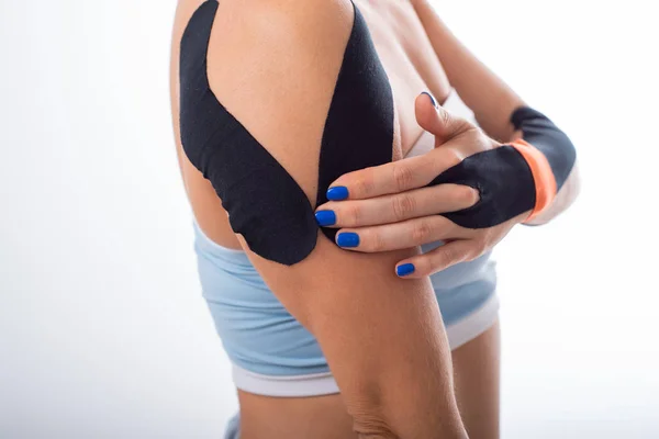 Female shoulder with kineziotape on a white background. Alternative medicine for sports injuries of joints and ligaments. Young sportswoman with medical record on a sore shoulder and wrist. — Stock Photo, Image