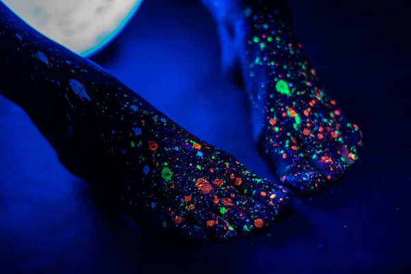 赤脚女性脚在油漆喷漆在黑暗中发光。荧光粉中的脚趾。身体艺术在紫外线下发光，像一片星空的蓝天。特写. — 图库照片