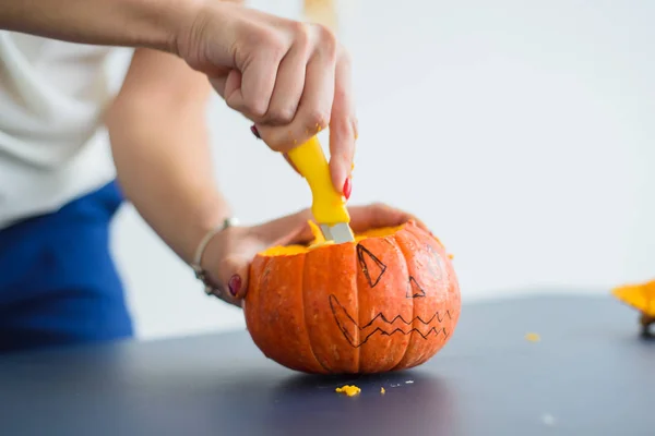 En kvinna karves hennes ansikte på en pumpa för en Halloween lampa på ett svart bord. Närbild kvinnliga händer gör Jack-o '-lykta till tröskeln till alla helgon.. — Stockfoto