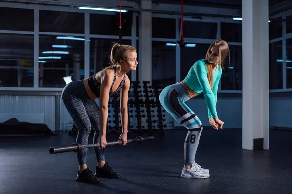 Joven chica de deportes hace callejón sin salida con una barra en el gimnasio bajo la supervisión de un entrenador. La entrenadora enseña a la sala de espera. Entrenamiento personal. Ejercicios en las nalgas . — Foto de Stock