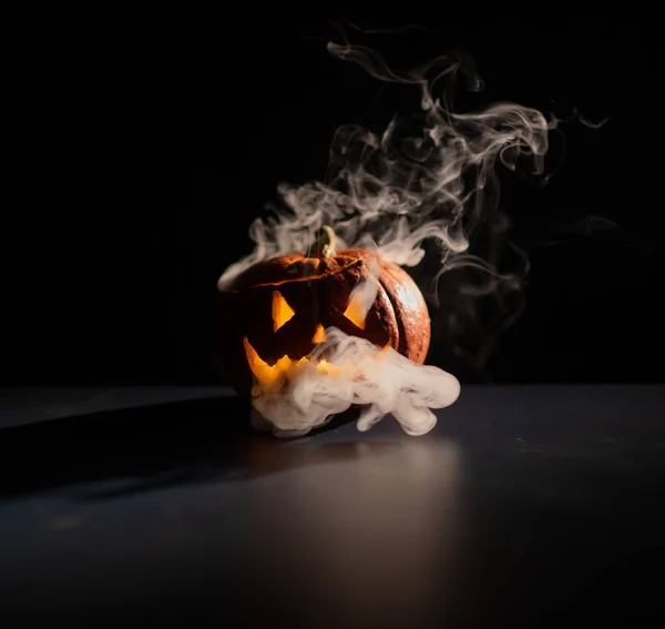 Halloween, oranje pompoen met een eng stralend gezicht op een donkere achtergrond. Grijze dikke rook komt uit. — Stockfoto