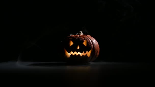Halloween, oranžová dýně s děsivou zářivou tváří na tmavém pozadí. Šedý hustý kouř vychází ven. — Stock video