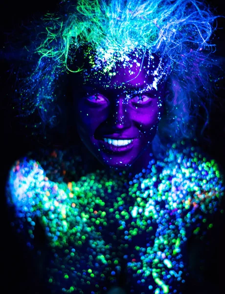 Body art and contact lenses glowing in ultraviolet light. Woman smiling, painted in fluorescent powder. Stars in the eyes