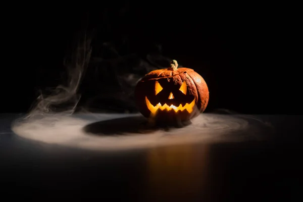 Halloween, apelsin pumpa med en skrämmande lysande ansikte på en mörk bakgrund. Grå tjock rök kommer ut. Närbild på Jack-o '-Lantern på tröskeln till alla helgon. — Stockfoto