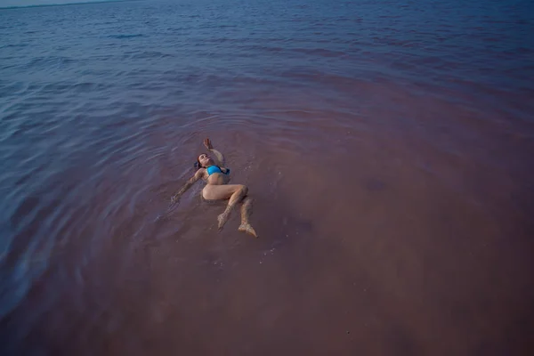 A woman in a blue bikini swims on her back in a salt lake. Miracle of nature pink lake. Deposit and extraction of salt. Dense water pushing to the surface. Therapeutic procedures in mineral water. — Stock Photo, Image