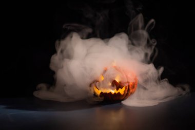 Cadılar Bayramı, koyu bir arka plan üzerinde korkutucu bir parlak yüzü ile turuncu kabak. Kalın gri duman çıkar ve siyah masa boyunca yayılır. Tüm azizlerin arifesinde bir el fenerinin yakın çekim