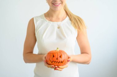 Beyaz bluz giymiş bir kadın Cadılar Bayramı için balkabağı tutuyor. All Saints arifesinde beyaz bir arka plan üzerinde bir fener jakı ile kadın ellerin yakın çekim. Ön plan. Hediye ver yoksa karışmam. Korkunç grimace.