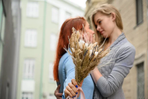 Relaţii de acelaşi sex. Cuplu lesbian fericit cu flori uscate. Două femei frumoase se îmbrățișează tandru unul pe altul la o întâlnire. Buchet în prim plan. Aproape de mână de cuplu. LGBT . — Fotografie, imagine de stoc