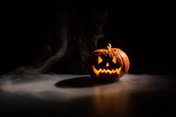 Halloween, apelsin pumpa med en skrämmande lysande ansikte på en mörk bakgrund. Tjock grå rök kommer ut och sprider sig över det svarta bordet. En närbild av en ficklampa på tröskeln till alla helgonen — Stockfoto