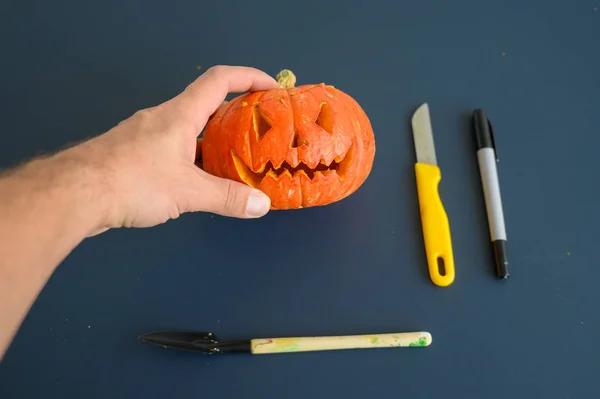 Frau hält einen kleinen Kürbis über schwarzem Hintergrund. Halloween-Konzept, flache Lage, Draufsicht. Kerze, Stift, Messer und Kürbis in der Hand auf einem schwarzen Tisch. — Stockfoto