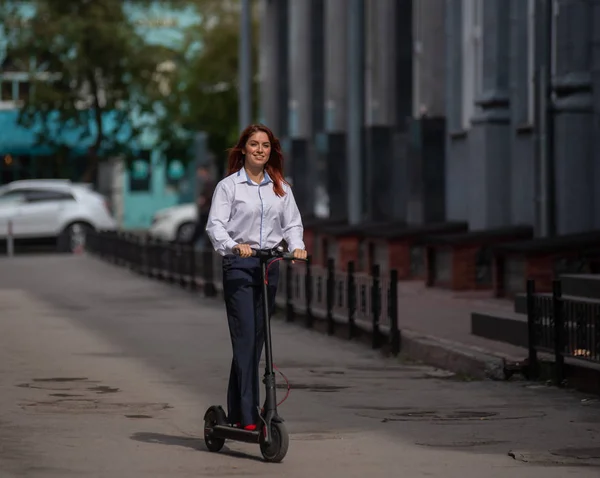 A red-haired girl in a white shirt drives an electric scooter along the wall. A business woman in a trouser suit and red high heels rides around the city in a modern car. dress code in the office.