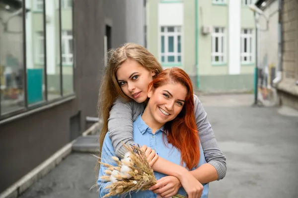 Gleichgeschlechtliche Beziehungen. glückliches lesbisches Paar mit getrockneten Blumen. umarmt das Mädchen die rothaarige Freundin sanft von hinten. in der Nähe eines Handpaares. lgbt — Stockfoto