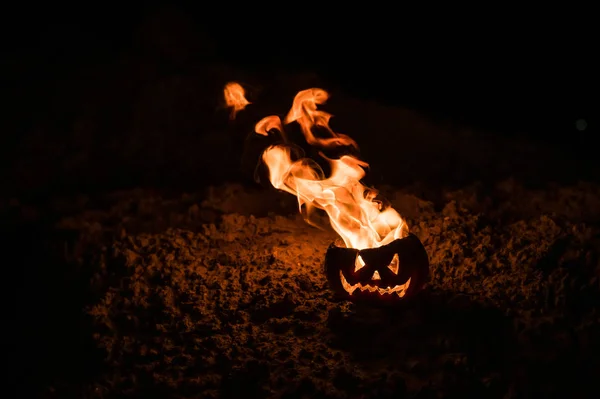 Tongen van vlam in een pompoen. Jack-o-lantern in brand op een zwarte achtergrond. Halloween symbool op de grond. Truc of behandelen. Close-up. — Stockfoto