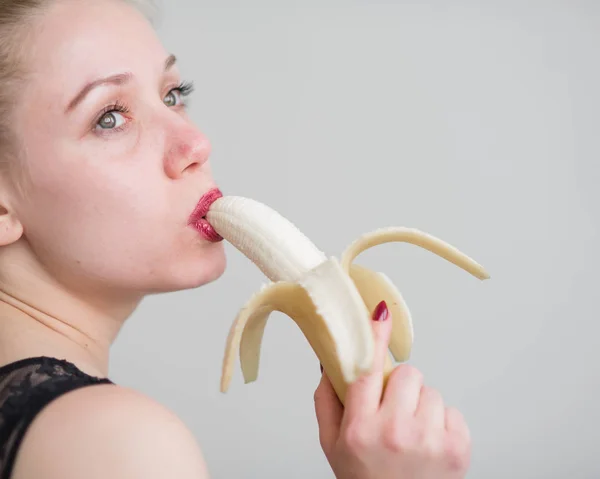 Une fille aux longs cheveux blonds lèche sexuellement une grosse banane jaune avec sa langue. Est le sexe oral — Photo