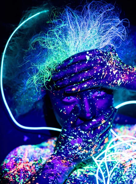 Body art e lenti a contatto che brillano nella luce ultravioletta. Ritratto di donna dipinta in polvere fluorescente. Stelle negli occhi. Nastro luce al neon . — Foto Stock