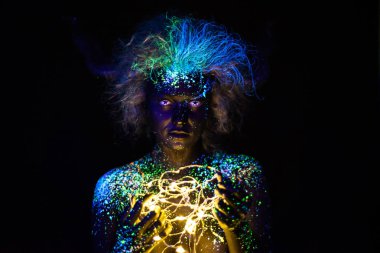 Vücut sanatı ve kontakt lensler ultraviyole ışıkta parlıyor. Floresan tozuyla boyanmış bir kadının portresi. Gözlerindeki yıldızlar. Neon ışık şerit.