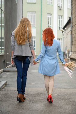 Gezinti. İki kız arkadaş el ele tutuşarak sokakta yürüyorlar. Kurutulmuş çiçek bir buket ile bir yürüyüş iki güzel kadının sırtları. buruşuk şeyler