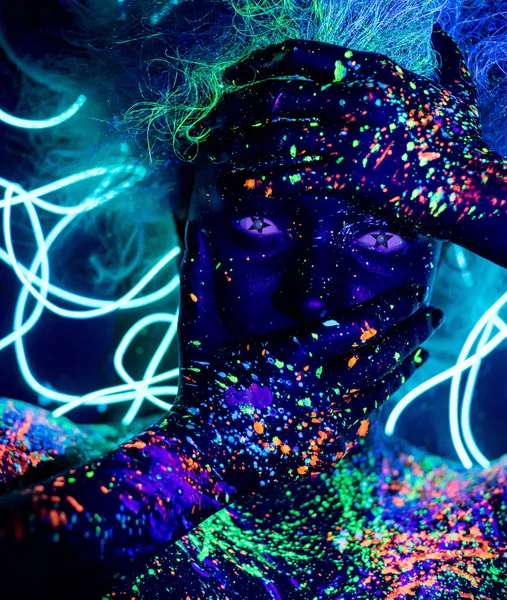 Body art and contact lenses glowing in ultraviolet light. Portrait of a woman painted in fluorescent powder. Stars in the eyes. Neon light ribbon.