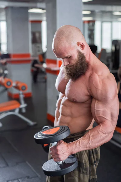 Bruut, gespierd, kaal met een baard atleet in de sportschool. Heft zware gewichten op, traint de biceps. Mooie borstspieren — Stockfoto