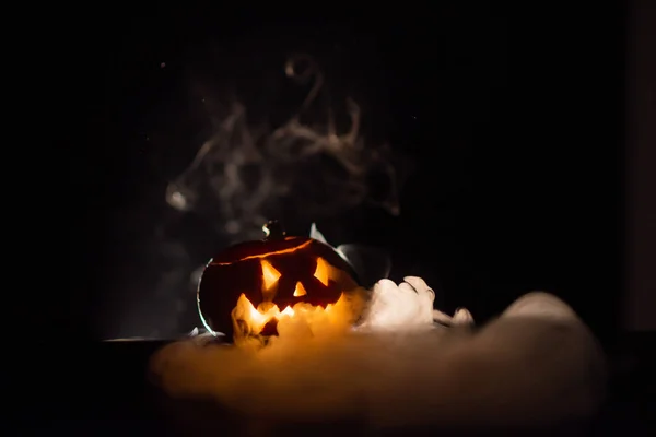 Halloween, orange pumpkin with a scary luminous face on a dark background. Thick gray smoke comes out and spreads across the black table. A close-up of a flashlight . Decorated candle stand. — Stock Photo, Image