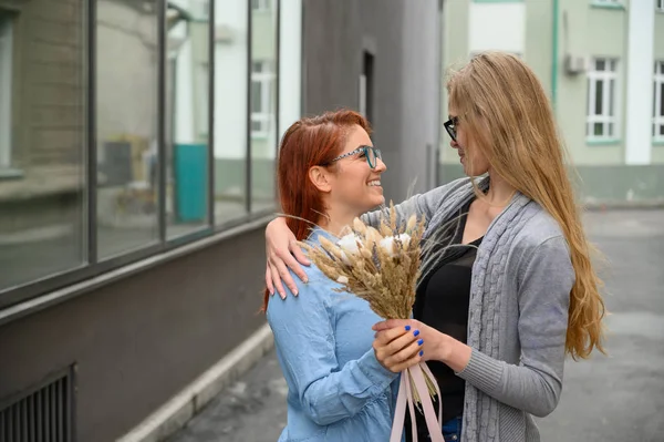 Same-sex relationships. Happy lesbian couple with dried flowers. Two beautiful women tenderly hug each other on a date. Bouquet in the foreground. Close up to couple hands.LGBT. — Stock Photo, Image