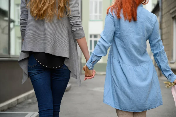 Relations homosexuelles. Joyeux couple lesbien marchant dans la rue en se tenant la main. Le dos de deux belles femmes à un rendez-vous avec un bouquet de fleurs séchées. LGBT . — Photo