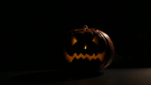 Halloween, orange pumpa med ett skrämmande glödande ansikte i mörkret. Tjockt grå rök kommer ut och sprider sig på det svarta bordet. En närbild av en blinkande ficklampa kvällen före alla helgon. — Stockvideo