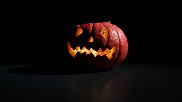 Halloween, oranžová dýně s děsivou zářivou tváří na tmavém pozadí. Vychází hustý šedý kouř a šíří se po černém stole. Detailní záběr baterky bez obalu v předvečer všech svatých — Stock video