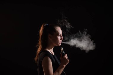 Esmer, siyah arka planda elektronik bir sigara içiyor ve ağzından yoğun bir duman salıyor. Bir kadın portresi sigara içiyor, havada süzülüyor..